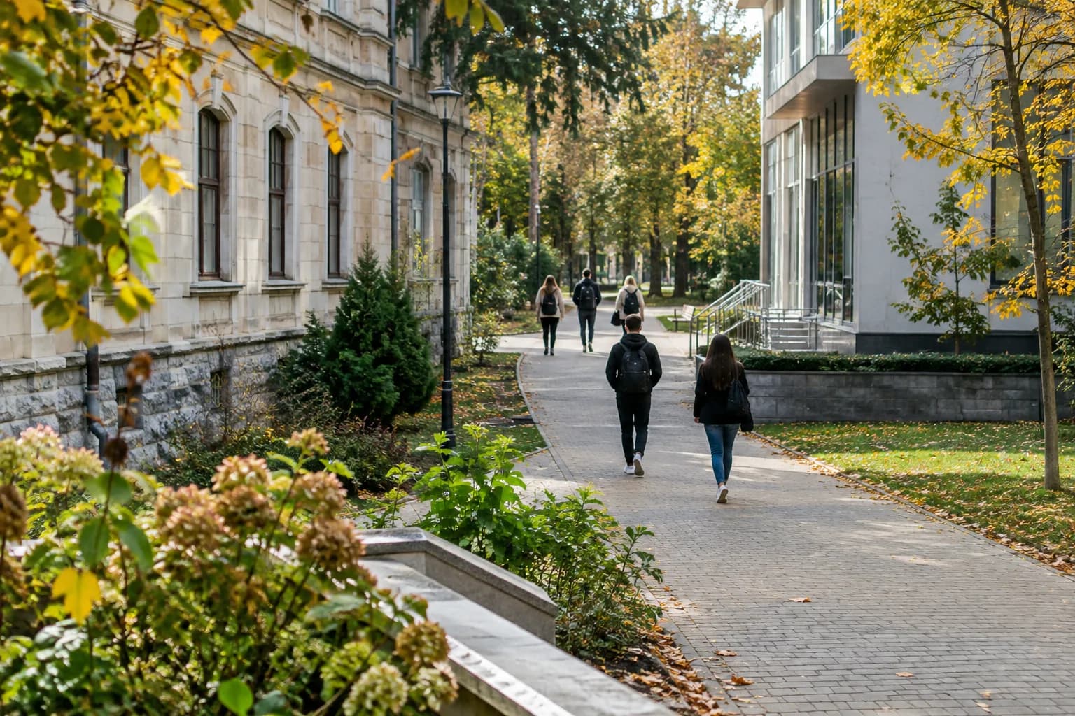 Young people seen from behind walk along a university campus path between older and newer buildings.