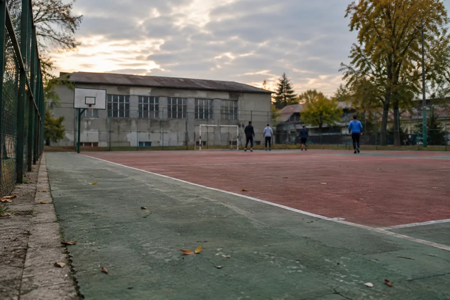 An outdoor sports court with a few people practising in the distance and a sports hall in the background.